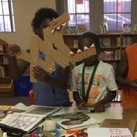 Children at Queen Memorial Library design impressive creations with cardboard and paper fasteners.